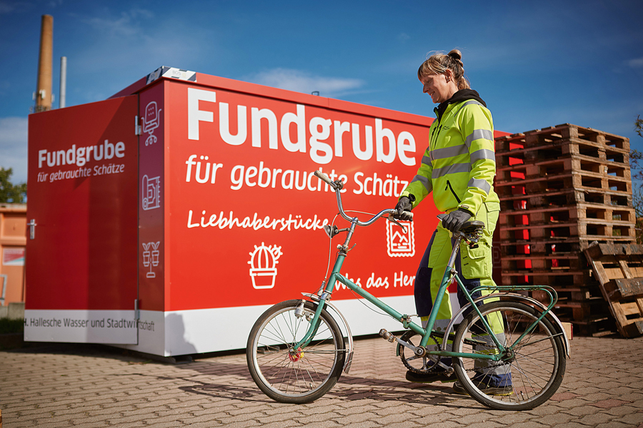 Eine Frau steht mit einem Fahrrad an der Fundgrube.