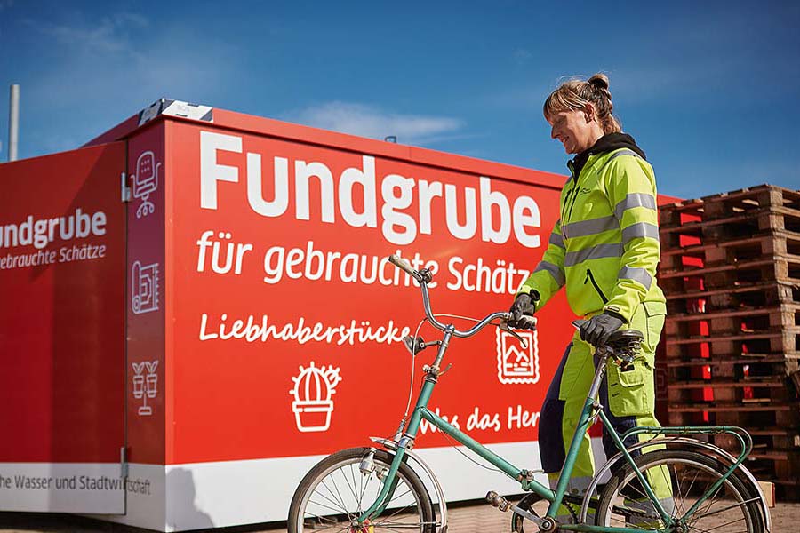 Eine Frau steht mit einem Fahrrad an der Fundgrube.