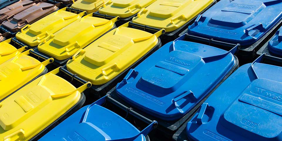 Blick von oben auf Abfalltonnen mit blauem, gelben und braunem Deckel.