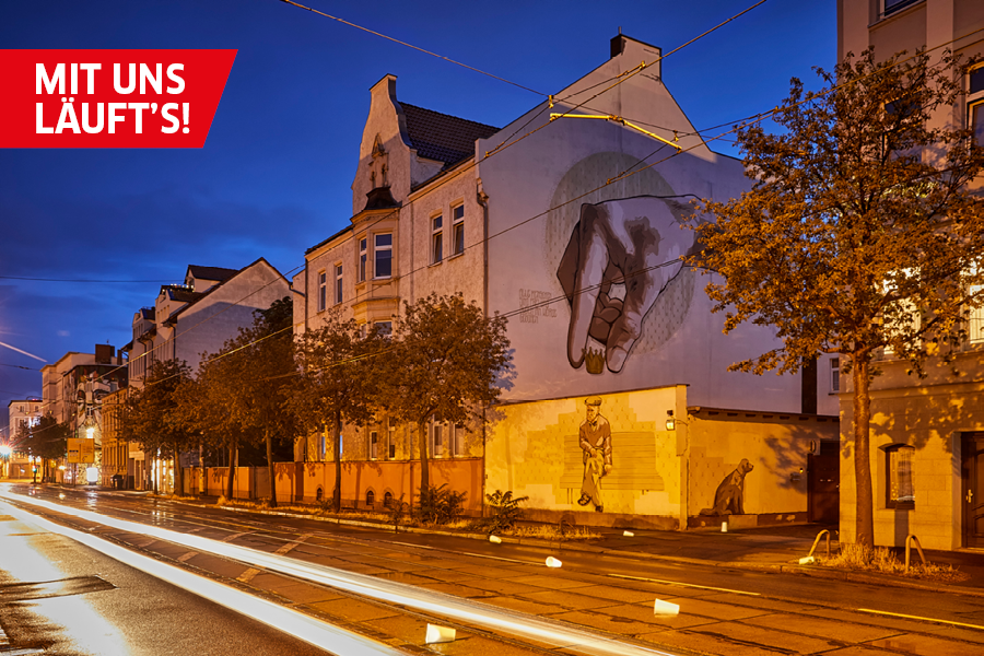 Das Bild zeigt die Freiraumgalerie in Halle/Freiimfelde bei Nacht. Die Straßenbeleuchtung gibt dem Bild eine Wärme. Plastikbecher liegen auf der Straße vor der Galerie.