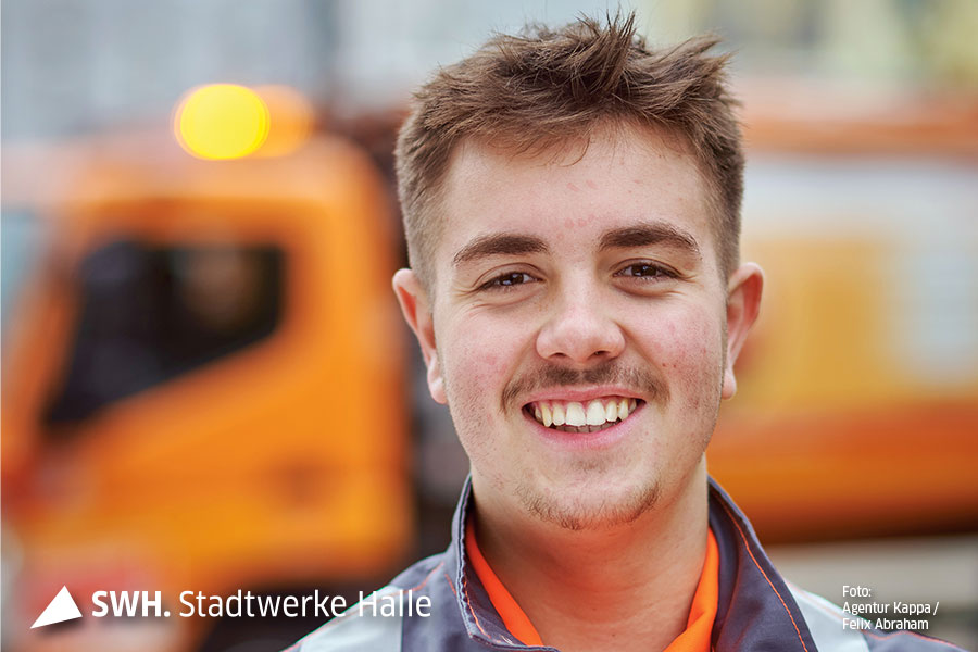 Ein junger man mit Drei-Tage-Bart lächelt in die Kamera. Er hat dunkelblonde Haare und trägt orangefarbene Arbeitsbekleidung der Halleschen Wasser und Stadtwirtschaft GmbH.