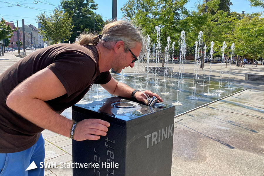 Ein HWS Mitarbeiter beugt sich über den neuen Trinkbrunnen am Steintor in Halle.